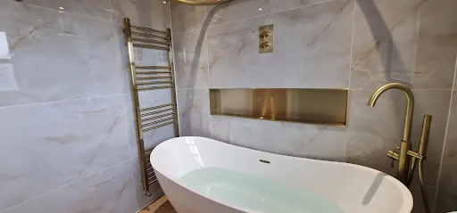 Freestanding bath with brass floor-standing tap and tiled niche
