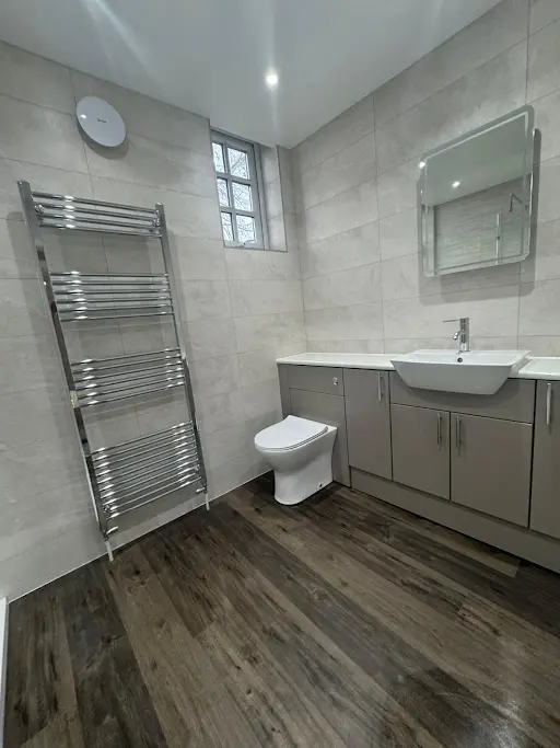 Fully tiled bathroom with vanity unit, chrome towel radiator and wood-effect flooring