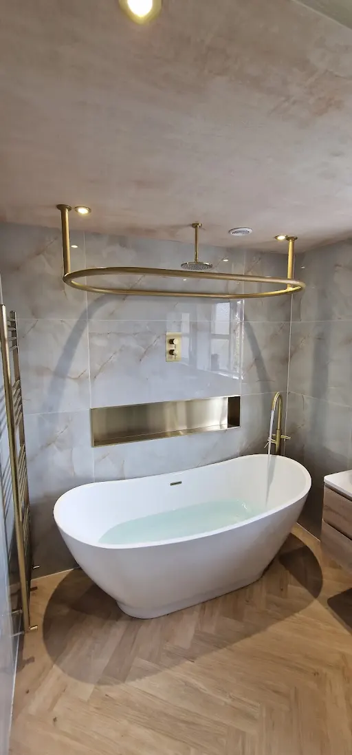 Freestanding bath with brushed brass ceiling shower ring and marble-effect tiling